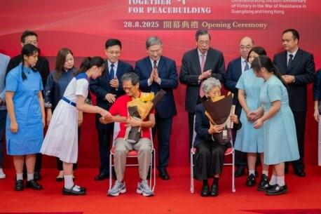 A group of people standing in front of a red wallDescription automatically generated